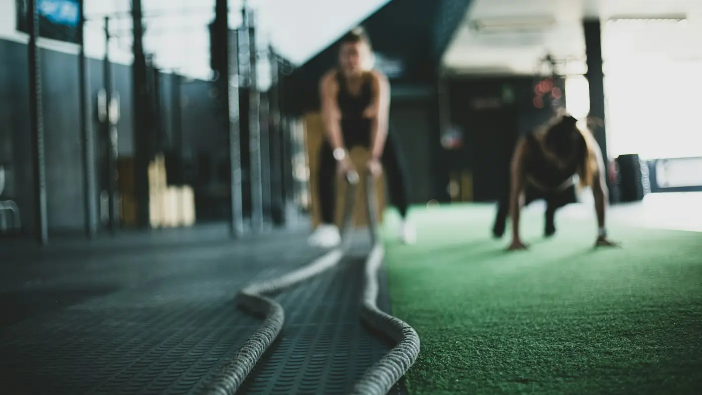 Two athletes training with battle ropes on a strip of green turf
