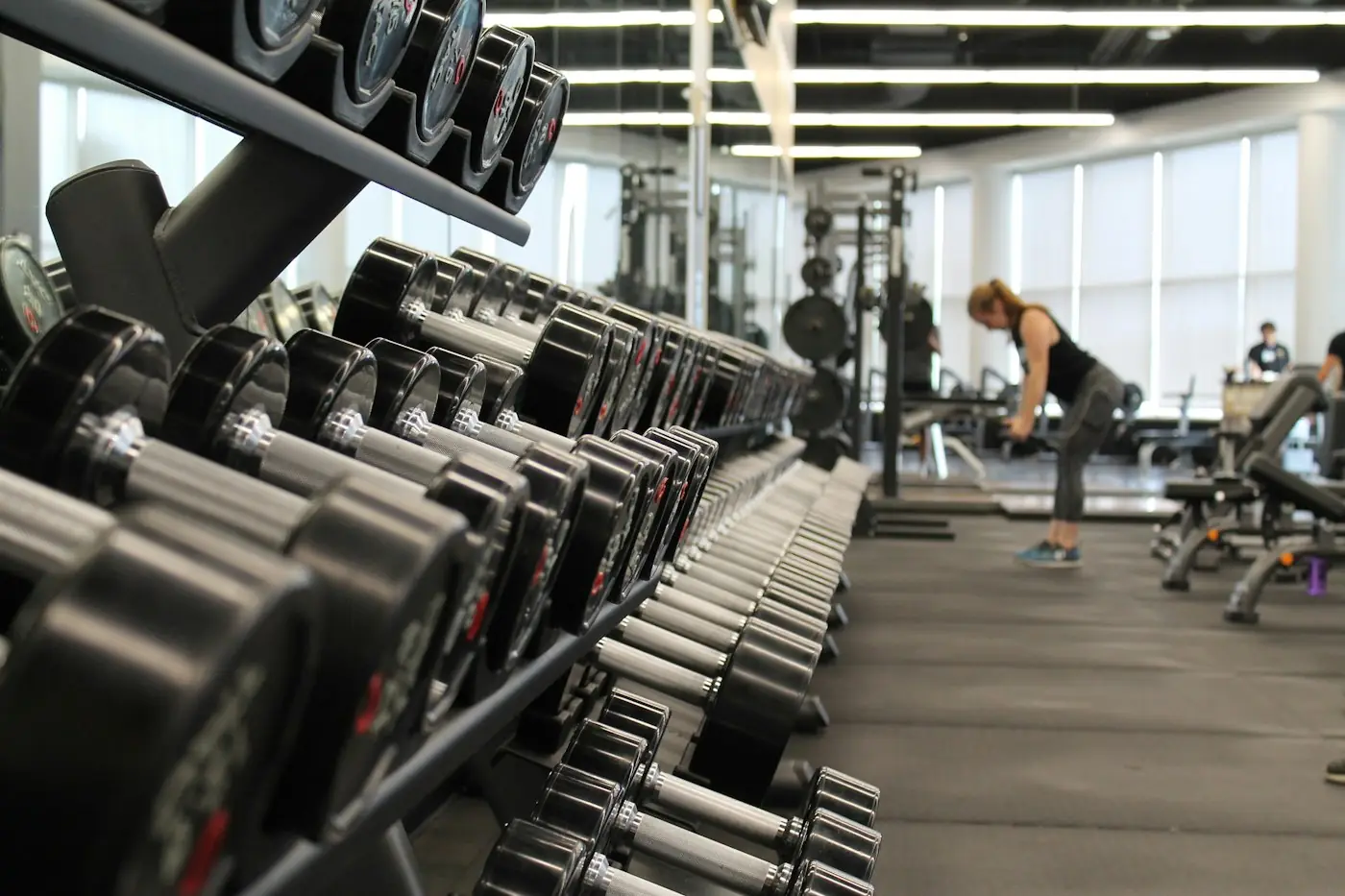 A long rack of black dumbbells in a bright, open gym