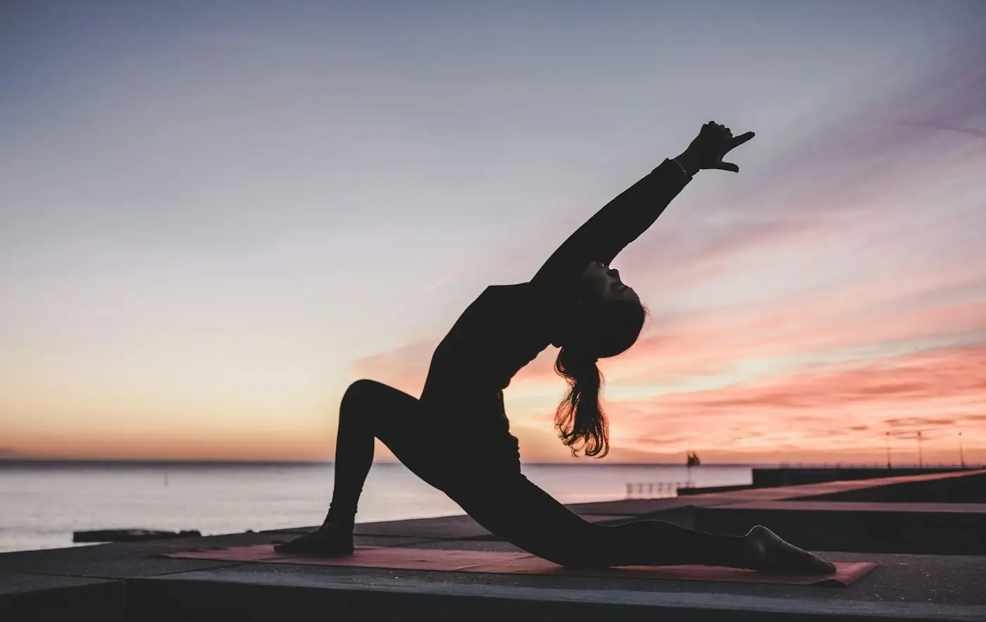 Silhouette of a person in a yoga pose against a pink and orange sunset sky
